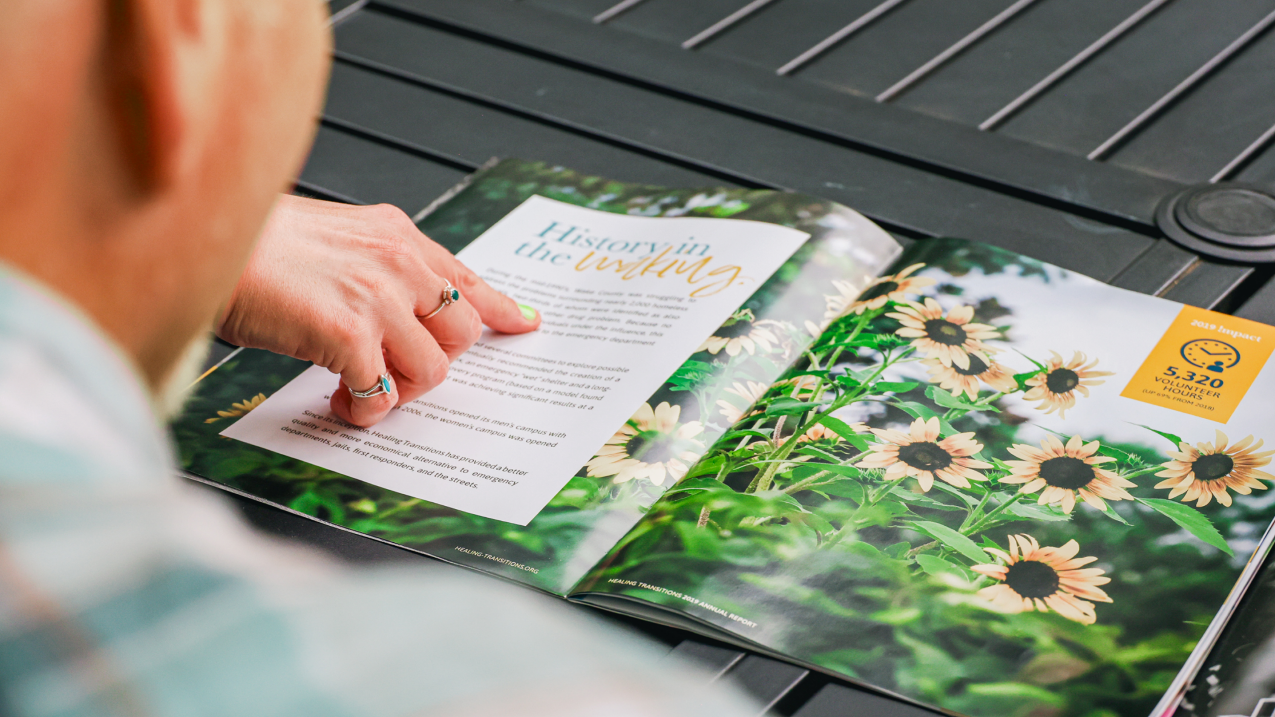 Person reading a nonprofit annual report featuring a "History in the Making" spread with sunflower photography and an impact statistic highlighting 5,220 volunteer hours.