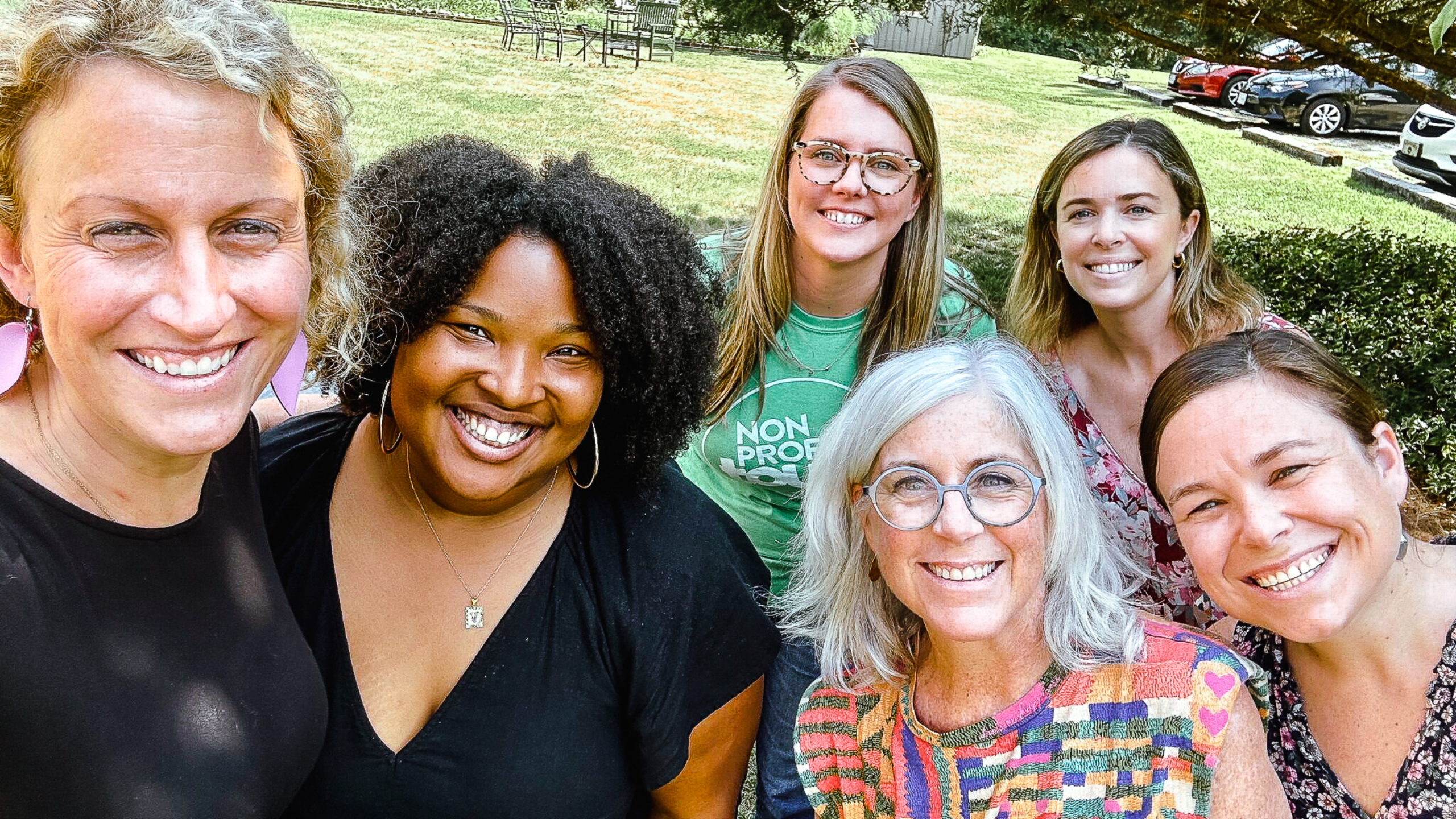 Four smiling members of the CARITAS team gathered outdoors for a group selfie in a grassy park with two smiling Angel Oak Creative team members.