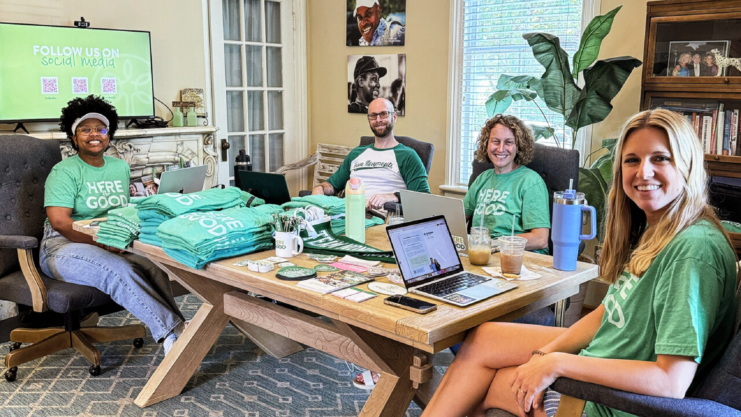 Angel Oak Creative team members gathered around a conference table during it's annual headshot day, wearing matching Here for Good shirts and surrounded by branded materials.