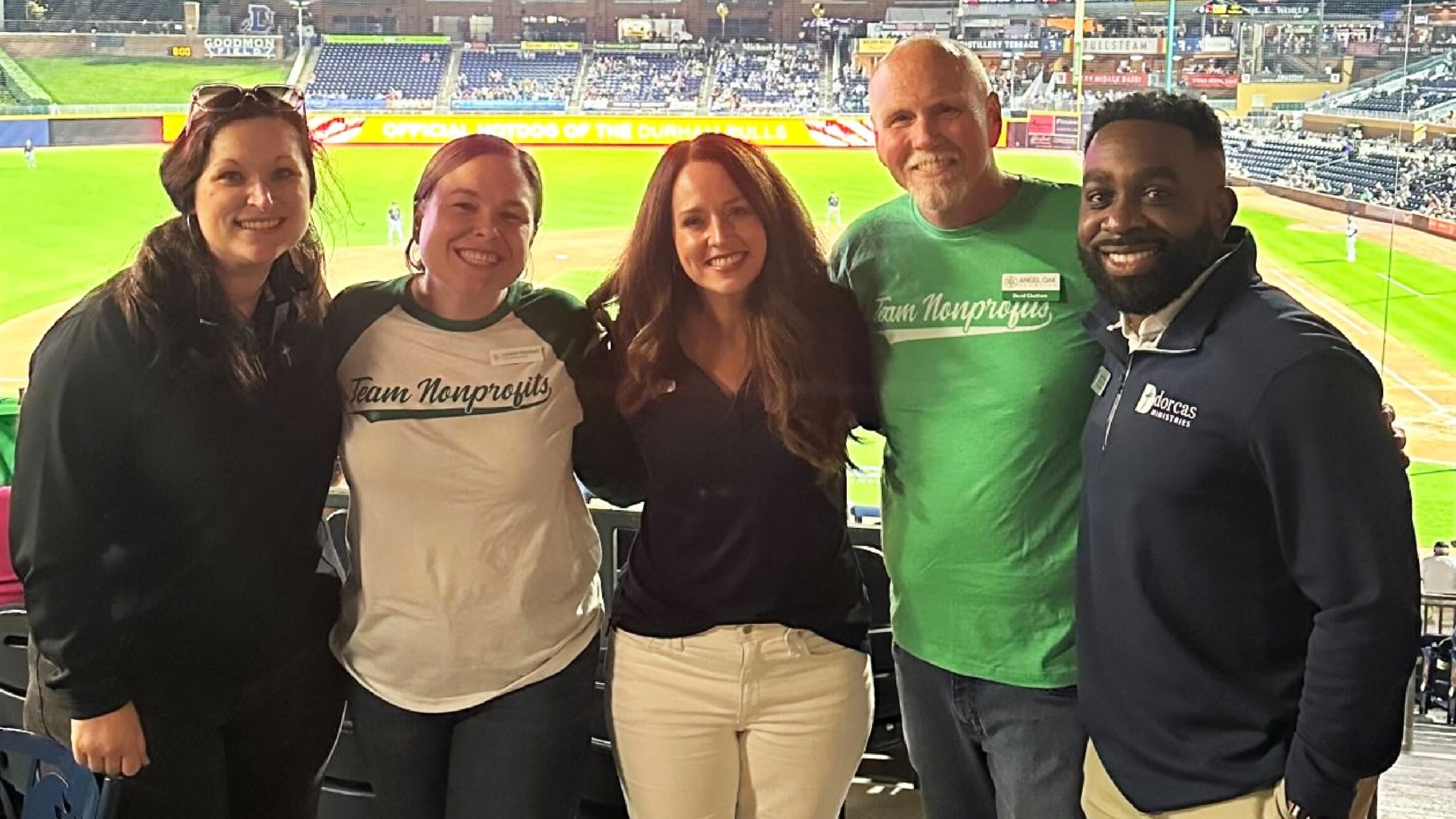Angel Oak Creative team members and a nonprofit client smiling together at a Durham Bulls baseball game networking event.